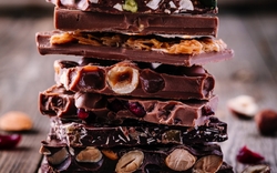 Stapel Vollmilch- und Zartbitterschokolade mit Nüssen, Karamell und Früchte und Beeren auf Holzhintergrund 