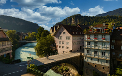 Stadtteil Heiligen Kreuz in Feldkirch, Österreich, mit historischen Gebäuden und einer Brücke über einen Fluss in einer malerischen Landschaft.