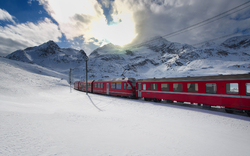 Ein roter Zug des Bernina Express fährt auf der Rhätischen Bahn durch die verschneiten Schweizer Alpen im Winter.