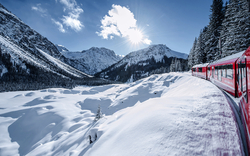 Roter Zug in winterlicher Alpenlandschaft mit Schnee und Sonne im Hintergrund.