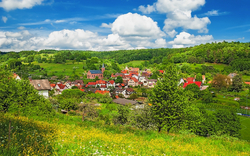 Dorf in grüner Landschaft mit blauen Himmel und Wolken.
