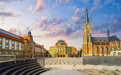 Theaterplatz in Chemnitz mit Blick auf das Opernhaus und die Petrikirche, umgeben von historischen Gebäuden unter einem leicht bewölkten Himmel.