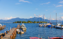 Ein Holzsteg mit mehreren Booten am Ufer eines Sees, im Hintergrund sind Berge zu sehen.