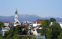 Rosenheim mit Gebäuden im Vordergrund und Bergen im Hintergrund.