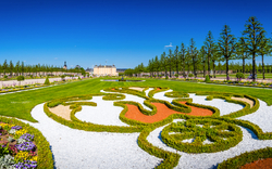 Ein symmetrischer Schlossgarten mit kunstvollen Beeten und blühenden Pflanzen.