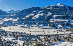 Panoramablick auf eine verschneite Stadt mit umgebenden Bergen und klarem blauem Himmel im Hintergrund.