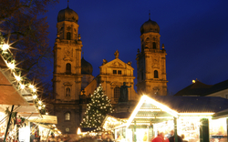 Weihnachtsmarkt mit beleuchteten Ständen und Kirche im Hintergrund bei Nacht