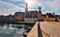 Historische Altstadt mit gotischer Kathedrale und farbenfrohen Gebäuden am Ufer eines Flusses, bei sonnigem Wetter.