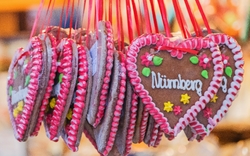 Lebkuchenherzen mit rot-weißer Zuckerglasur und dekorativen Blumen, die an roten Bändern aufgehängt sind. Auf einem Herz steht das Wort 