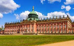 Neues Palais im Park Sanssouci in Potsdam, Deutschland, eine barocke Schlossanlage mit blauem Himmel und Wolken im Hintergrund.
