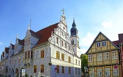 Historisches Fachwerkgebäude in der Celler Altstadt in Niedersachsen, Deutschland, mit dem Alten Rathaus im Vordergrund und einem blauen Himmel im Hintergrund.