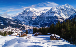 Blick auf die verschneite Landschaft von Grindelwald in der Jungfrauregion der Berner Alpen, mit dem Berg Wetterhorn im Hintergrund, umgeben von Chalets und einem Wintersportgebiet.