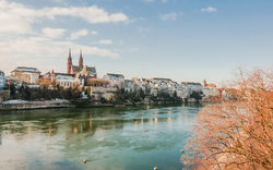 Blick auf die Altstadt von Basel im Winter, mit dem Rhein im Vordergrund und dem Basler Münster im Hintergrund.