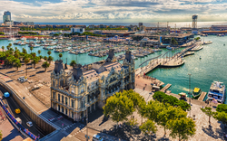 Hafen von Barcelona mit historischem Gebäude und Yachten im Wasser.