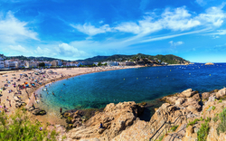 Panoramablick auf einen belebten Strand mit blauem Himmel und klarem Meerwasser.