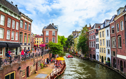 Kanal in einer Stadt mit Häusern, Bäumen und Menschen auf einer Terrasse.