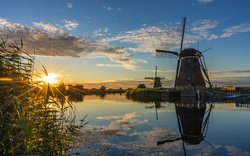 Windmühlen bei Sonnenuntergang mit Spiegelung im Wasser, umgeben von Schilf.