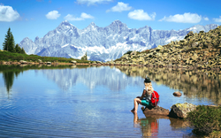 Frau sitzt am See mit Blick auf Berglandschaft und klaren Himmel.