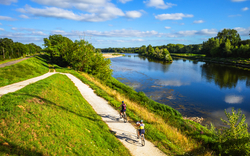 Radfahrer auf einem Weg entlang eines Flusses bei sonnigem Wetter.