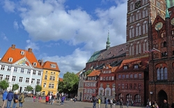 Backsteinkirche St. Nikolai in Stralsund mit historischem Platz und Besuchern bei Sonnenschein.