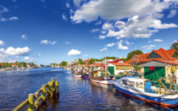 Hafen mit Fischerbooten, bunten Häusern und blauem Himmel mit einigen Wolken.