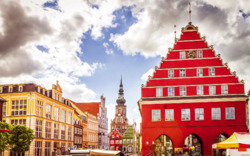 Historischer Marktplatz mit roten Giebelhäusern und Kirchturm im Hintergrund.