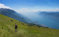 Wanderer auf grünem Hügel mit Blick auf See und Berge im Hintergrund.