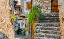 Steingasse in einem historischen Dorf mit Blumen und einer bemalten Hausfassade.
