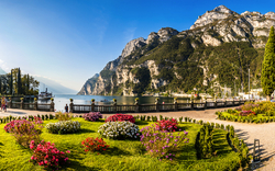 Gepflegte Gartenanlage am Ufer eines Sees mit Bergen im Hintergrund.