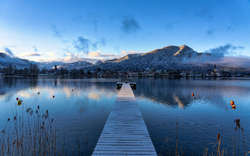 Tegernsee im Winter mit schneebedeckten Bergen im Hintergrund und einem Steg, der ins ruhige Wasser führt.