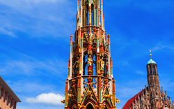 Bunter gotischer Brunnen vor einem blauen Himmel in einer Stadtumgebung.
