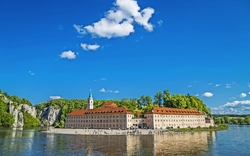 Historische Klosteranlage an einem Fluss unter blauem Himmel mit Wolken.
