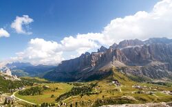 Berglandschaft mit grünen Wiesen, Wanderwegen und bewölktem Himmel in den Alpen.