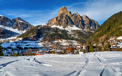 Verschneite Berglandschaft mit Dorf im Tal, Dolomiten im Hintergrund.