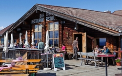 Restaurant auf Berghütte mit Sonnenterrasse und Gästen bei gutem Wetter.