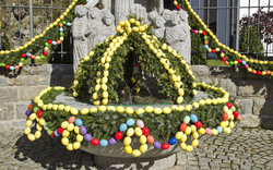 Osterbrunnen mit buntem Osterschmuck aus Eiern und Grünzweigen.