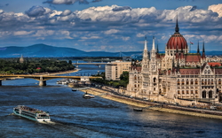 Parlament von Budapest am Ufer der Donau, mit Schiff und Brücke im Hintergrund.