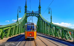 Straßenbahn fährt über grüne Brücke an einem sonnigen Tag.
