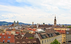 Panoramablick auf die Stadt Linz mit Kirchtürmen und bewölktem Himmel.