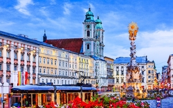 Historischer Platz mit Kirche, Straßenbahn und Blumen im Vordergrund bei Dämmerung.