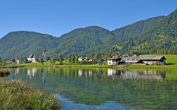 Landschaft mit Dorf am See, umgeben von grünen Bergen.