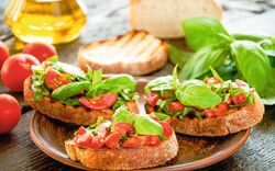 Drei Bruschetta-Scheiben mit Tomaten und Basilikum auf einem Teller.