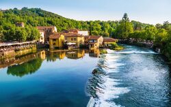 Malersiches Dorf am Fluss mit gelben Häusern, umgeben von grünen Bäumen.