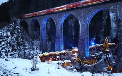 Weihnachtsmarkt unter einer Eisenbahnbrücke im Schnee, mit beleuchtetem Baum.