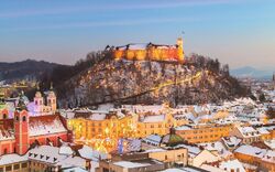 Winterliche Stadtansicht mit einer beleuchteten Burg auf einem Hügel im Hintergrund.