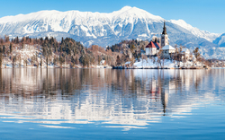 Winterliche Seelandschaft mit Bergen und Kirche, Bled, Slowenien.
