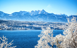 Verschneite Landschaft mit See und Bergen im Hintergrund.