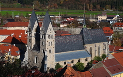 Stadtansicht mit einer großen Kirche im Vordergrund und Hügeln im Hintergrund.