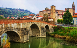 Steinbrücke über Fluss mit historischen Gebäuden im Hintergrund.