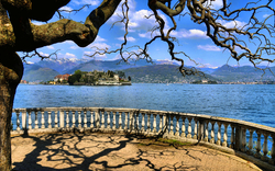 Blick auf Insel in See mit Bergen, von Terrasse mit Baum, blauer Himmel.